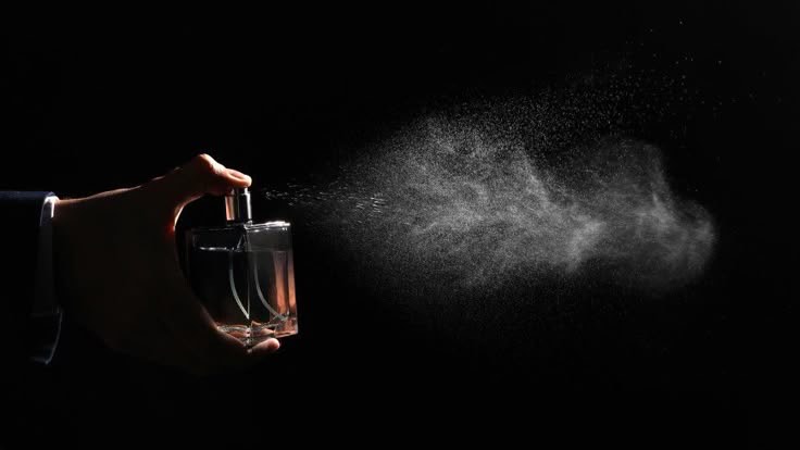 Mano rociando perfume, frasco de vidrio. Una nube de vapor se dispersa sobre fondo negro